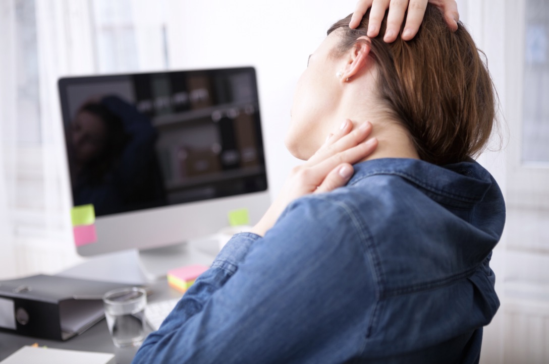 Woman in front of computer screen stretching sore neck